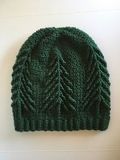 a green knitted beanie with trees on the front and sides, sitting on a white surface