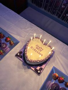 a birthday cake with lit candles sitting on top of a table next to other desserts