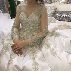 a woman sitting on top of a bed wearing a white dress with gold embroiderys