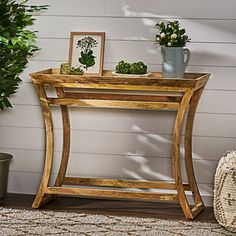 a wooden table sitting next to a potted plant on top of a rug in front of a white wall