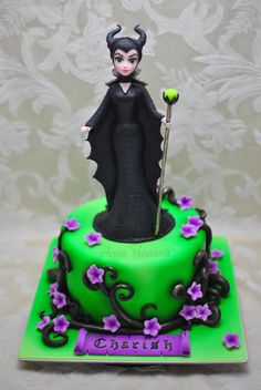 a green cake with a maleficent figure on top and purple flowers around the edges