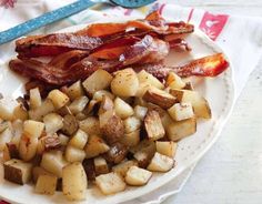 a white plate topped with potatoes and bacon on top of a table next to utensils