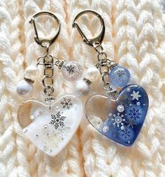 two heart shaped key chains with snowflakes and pearls hanging from them on a white knitted surface