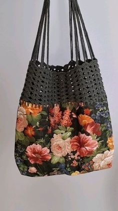 a purse hanging from a hook with flowers on it and black crochet handles