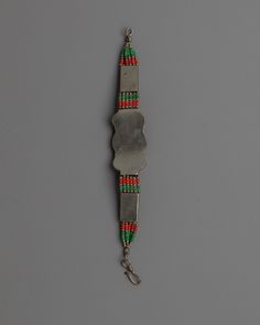 a metal object with red, green and orange beads on it's side hanging from a chain