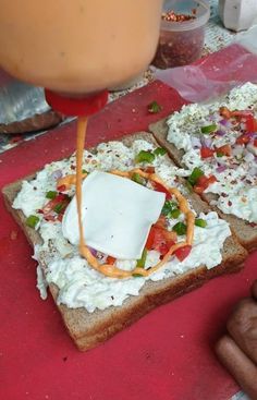 someone is spreading cheese on top of a piece of bread with other food in the background