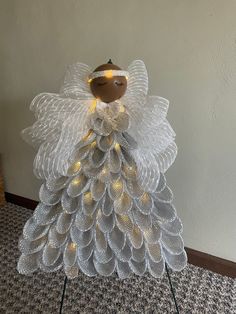 an angel made out of mesh with lights on it's head and wings, standing in front of a wall