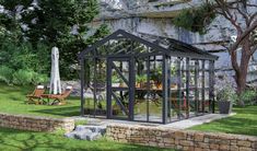 a small glass house sitting on top of a lush green field next to a stone wall