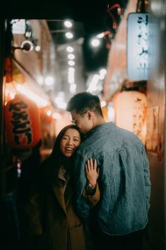 a man and woman embracing each other in an alleyway with lights on the walls