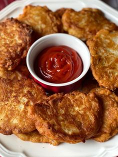 some fried food on a white plate with ketchup and dipping sauce in the middle