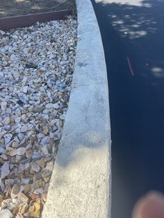 there is a cat that is sitting on the edge of a sidewalk next to some rocks