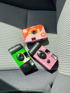 two cameras sitting on the back seat of a car, one pink and one green