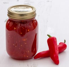 a jar of red peppers sitting on top of a white table next to a pepper