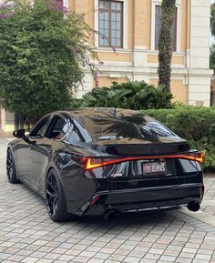 a black sports car is parked in front of a large building with trees and bushes