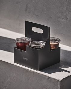 two plastic cups sitting in a black box next to each other on a concrete ledge