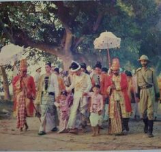 a group of people standing next to each other on a dirt road with an umbrella