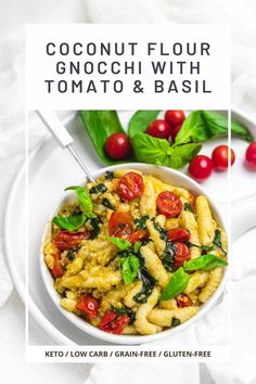 a white bowl filled with pasta and spinach on top of a table next to cherry tomatoes