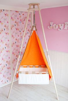 a baby's room with pink walls and floral wallpaper, including an orange teepee