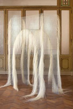 an art work with long white hair on the floor and in front of a wall