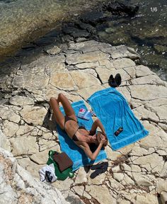 a woman laying on top of a rock next to a body of water with a towel