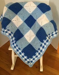 a blue and white crocheted blanket sitting on top of a wooden chair next to a wall