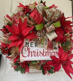 a christmas wreath with red poinsettis and green ribbon hanging on a door