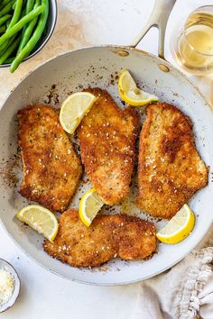 fried fish with lemons and green beans in a skillet on a white table