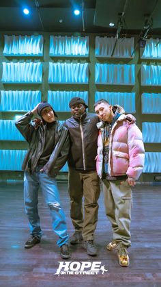 three young men standing next to each other in front of a wall with blue lights