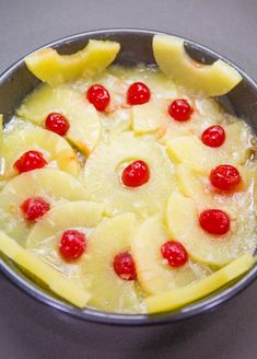 a bowl filled with pineapples and cherries on top of a gray table