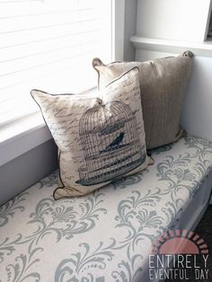 two pillows sitting on top of a bench next to a window