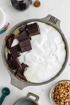 a pan filled with chocolate and nuts on top of a white counter next to a bottle of wine