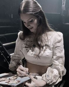 a woman sitting at a table with a book in her lap and writing on the paper