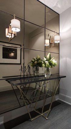 a glass table with vases and flowers on it in front of a large mirror