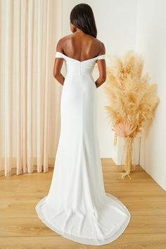 the back of a woman in a white wedding dress standing on a wooden floor next to a plant