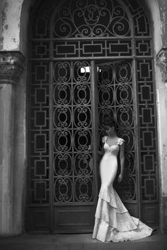 a woman standing in front of an iron door wearing a dress with ruffles