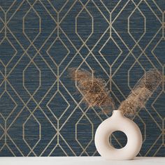 a white vase sitting on top of a table next to a wallpapered background