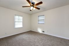 an empty room with two windows and a ceiling fan in the corner on the far wall