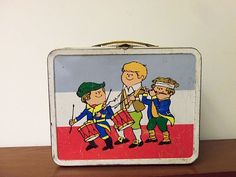 an old tin lunch box with children playing on the front and side panels painted to look like they're marching