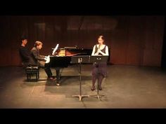 two people sitting at a piano and one standing in front of the piano on stage