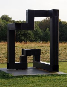 an abstract sculpture in the middle of a grassy field with trees in the back ground