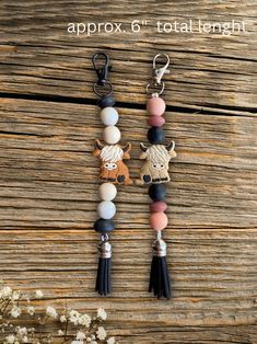 two key chains with charms on them sitting next to each other in front of a wooden background