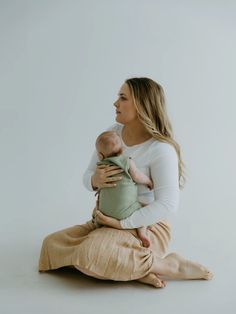 a woman sitting on the floor holding a baby in her arms and looking off into the distance