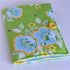 a green and blue flowered notebook with a yellow button