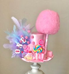 a pink hat with candy, lollipops and candies on it sitting on top of a white pedestal