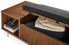 a wooden bench with a black cushion on top and some books in the bottom drawer