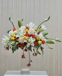 a vase filled with lots of white and orange flowers on top of a table next to a wall