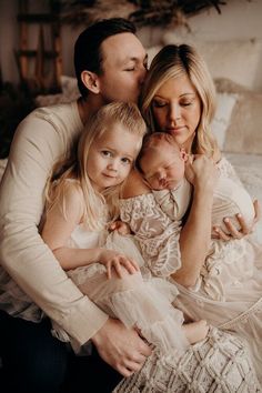 a woman, man and two children are sitting on a bed with their arms around each other