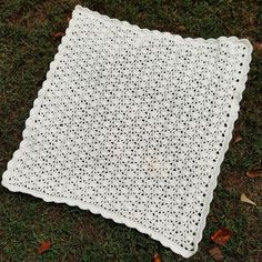 a white crocheted blanket laying on top of the grass with leaves around it