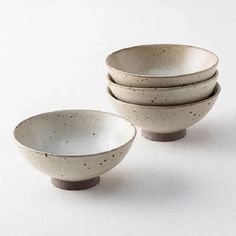 four white bowls sitting on top of each other in front of a white background with black speckles