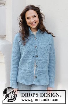 a woman standing in front of a white wall wearing a blue cardigan and smiling